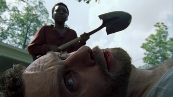 Movie still from “The Walking Dead” (2010), directed by Daniel Sackheim – A man with a beard is laying on the ground with a shovel in front of him and another man is standing behind him; Close Up shot, Over the shoulder angle