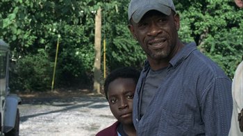 Movie still from “The Walking Dead” (2010), directed by Daniel Sackheim – A man and a young boy standing next to each other in a wooded area; Medium shot, Over the shoulder angle