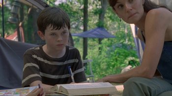 Movie still from “The Walking Dead” (2010), directed by Daniel Sackheim – A woman and a boy sitting at a table with a book; Close Up shot, High angle
