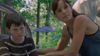 Movie still from “The Walking Dead” (2010), directed by Daniel Sackheim – A woman sitting next to a young boy in front of trees; Medium shot, Over the shoulder angle