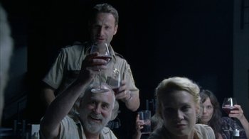 Movie still from “The Walking Dead” (2010), directed by Daniel Sackheim – A group of people holding wine glasses in front of a dark background; Medium shot, Low angle