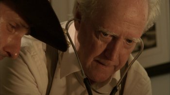 Movie still from “The Walking Dead” (2010), directed by Daniel Sackheim – An older man wearing a stethoscope looking at the camera; Close Up shot, Low angle