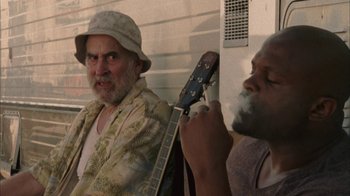 Movie still from “The Walking Dead” (2010), directed by Daniel Sackheim – A man sitting next to another man holding a guitar; Medium shot, Over the shoulder angle