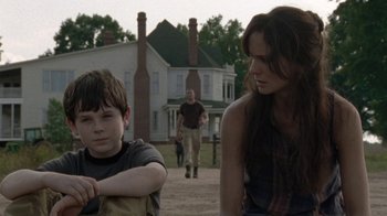 Movie still from “The Walking Dead” (2010), directed by Daniel Sackheim – A woman standing next to a boy in front of a house; Medium shot, Over the shoulder angle