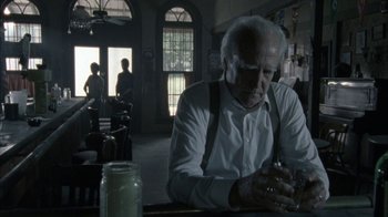 Movie still from “The Walking Dead” (2010), directed by Daniel Sackheim – An older man sitting at a table looking at his cell phone; Medium shot, Over the shoulder angle