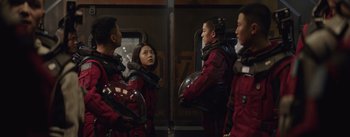 Movie still from “The Wandering Earth” (2019), directed by Frant Gwo – A group of people in red suits standing next to each other on a train; Medium shot, Over the shoulder angle
