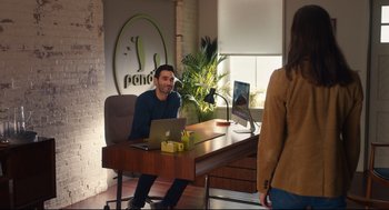 Movie still from “Can You Keep a Secret?” (2019), directed by Elise Durán – A man sitting in front of a laptop computer on top of a wooden desk; Wide shot, Over the shoulder angle