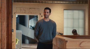 Movie still from “Can You Keep a Secret?” (2019), directed by Elise Durán – A man standing in front of a wall in a room; Medium shot, Over the shoulder angle