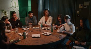 Movie still from “Can You Keep a Secret?” (2019), directed by Elise Durán – A group of people sitting around a table at a restaurant; Medium shot, High angle