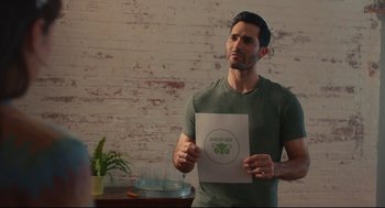 Movie still from “Can You Keep a Secret?” (2019), directed by Elise Durán – A man standing in front of a brick wall holding a paper; Medium shot, Over the shoulder angle