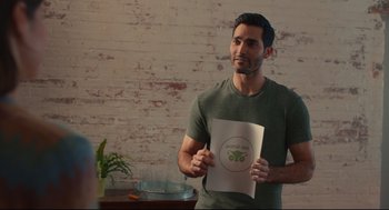 Movie still from “Can You Keep a Secret?” (2019), directed by Elise Durán – A man standing in front of a brick wall holding a paper; Medium shot, Over the shoulder angle