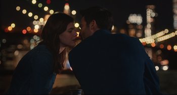 Movie still from “Can You Keep a Secret?” (2019), directed by Elise Durán – A man and a woman kissing at a table in front of lights; Medium shot, Over the shoulder angle