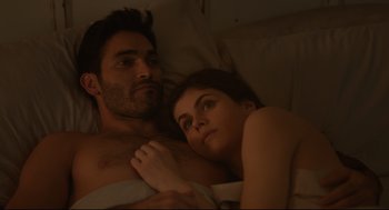 Movie still from “Can You Keep a Secret?” (2019), directed by Elise Durán – A man and a woman laying in bed together; Medium shot, Overhead angle