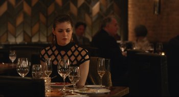 Movie still from “Can You Keep a Secret?” (2019), directed by Elise Durán – A woman sitting at a table with a glass of wine; Medium shot, Over the shoulder angle