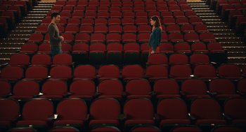 Movie still from “Can You Keep a Secret?” (2019), directed by Elise Durán – Two people are standing in an empty auditorium; Extreme Wide shot, High angle