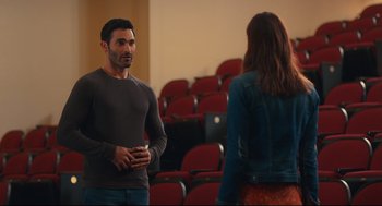 Movie still from “Can You Keep a Secret?” (2019), directed by Elise Durán – A man and a woman are standing in front of red chairs; Medium shot, Over the shoulder angle