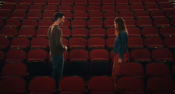 Movie still from “Can You Keep a Secret?” (2019), directed by Elise Durán – A man and a woman standing in front of rows of red seats; Wide shot, High angle