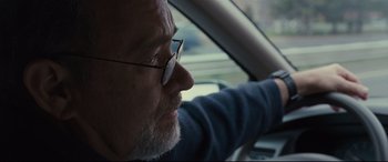 Movie still from “Captain Phillips” (2013), directed by Paul Greengrass – An older man wearing glasses sitting in the driver's seat of a car; Close Up shot, Over the shoulder angle