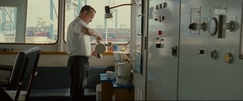 Movie still from “Captain Phillips” (2013), directed by Paul Greengrass – A man in a white shirt and black pants is pouring something into a cup; Medium shot, High angle