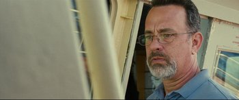 Movie still from “Captain Phillips” (2013), directed by Paul Greengrass – A man with a beard wearing glasses looking out a window; Close Up shot, Low angle