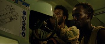 Movie still from “Captain Phillips” (2013), directed by Paul Greengrass – A man is driving a car in the back of a vehicle; Close Up shot, Over the shoulder angle