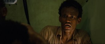 Movie still from “Captain Phillips” (2013), directed by Paul Greengrass – A man in a brown shirt is looking at the camera; Close Up shot, High angle