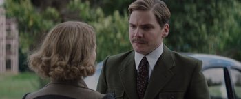 Movie still from “The Zookeeper's Wife” (2017), directed by Niki Caro – A man in a suit and tie talking to a woman in front of bushes; Close Up shot, Over the shoulder angle