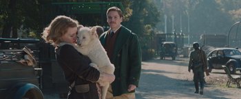 Movie still from “The Zookeeper's Wife” (2017), directed by Niki Caro – A man holding a white dog in his arms; Medium shot, Over the shoulder angle