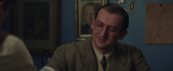 Movie still from “The Zookeeper's Wife” (2017), directed by Niki Caro – A man in a suit and tie sitting in front of a painting; Close Up shot, Over the shoulder angle