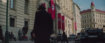 Movie still from “The Zookeeper's Wife” (2017), directed by Niki Caro – A man walking down the street in front of a building with nazi flags; Wide shot, Low angle
