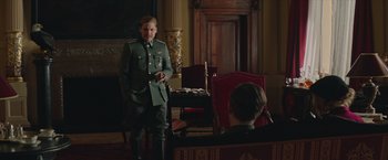Movie still from “The Zookeeper's Wife” (2017), directed by Niki Caro – A man in a military uniform standing in front of a chair; Medium shot, Over the shoulder angle