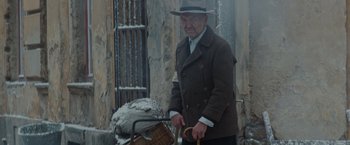 Movie still from “The Zookeeper's Wife” (2017), directed by Niki Caro – An older man in a hat and coat holding a basket; Medium shot, Over the shoulder angle