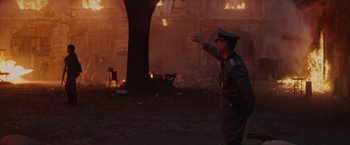 Movie still from “The Zookeeper's Wife” (2017), directed by Niki Caro – A man in a military uniform standing in front of a burning building; Wide shot, Over the shoulder angle