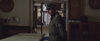 Movie still from “The Zookeeper's Wife” (2017), directed by Niki Caro – A man in a military uniform standing next to a table; Medium shot, Low angle