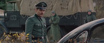 Movie still from “The Zookeeper's Wife” (2017), directed by Niki Caro – A man in a military uniform standing next to a car; Medium shot, Low angle