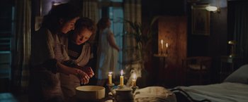Movie still from “The Zookeeper's Wife” (2017), directed by Niki Caro – A woman lighting candles on a cake in front of a window; Medium shot, Over the shoulder angle