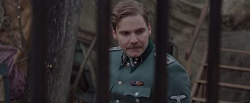 Movie still from “The Zookeeper's Wife” (2017), directed by Niki Caro – A man in a military uniform standing behind a fence; Close Up shot, Low angle