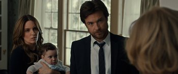 Movie still from “This Is Where I Leave You” (2014), directed by Shawn Levy – A man wearing a suit and tie holding a baby in his arms; Close Up shot, Over the shoulder angle