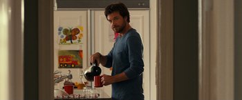 Movie still from “This Is Where I Leave You” (2014), directed by Shawn Levy – A man pouring a cup of coffee into a red mug; Medium shot, Over the shoulder angle