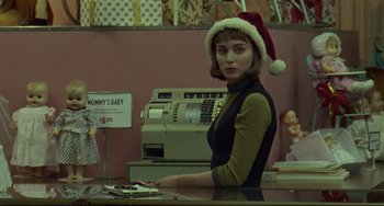 Movie still from “Carol” (2015), directed by Todd Haynes – A woman wearing a santa clause hat stands behind a cash register; Medium shot, Over the shoulder angle