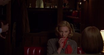 Movie still from “Carol” (2015), directed by Todd Haynes – A woman sitting in a booth holding a cell phone to her ear; Medium shot, Over the shoulder angle