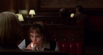 Movie still from “Carol” (2015), directed by Todd Haynes – A woman sitting at a table with a cigarette in her mouth; Medium shot, Over the shoulder angle