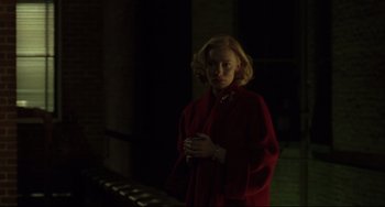 Movie still from “Carol” (2015), directed by Todd Haynes – A woman in a red coat standing in a dark room; Medium shot, Over the shoulder angle
