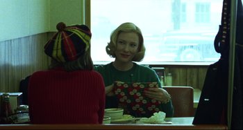 Movie still from “Carol” (2015), directed by Todd Haynes – Two women are sitting at a table with a present; Medium shot, Over the shoulder angle
