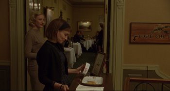 Movie still from “Carol” (2015), directed by Todd Haynes – A woman standing at a table with a sandwich in front of her; Medium shot, Over the shoulder angle