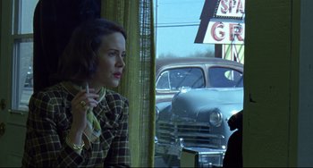 Movie still from “Carol” (2015), directed by Todd Haynes – A woman sitting in front of an open window with an old car in the background; Medium shot, Over the shoulder angle