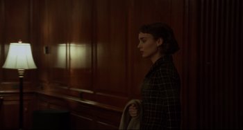 Movie still from “Carol” (2015), directed by Todd Haynes – A woman standing in front of a wooden wall holding a blanket; Medium shot, Over the shoulder angle