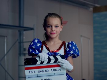 Movie still from “Casting JonBenet” (2017), directed by Kitty Green – A young girl holding a clapperboard in her hands; Medium shot, High angle