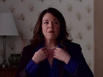 Movie still from “Casting JonBenet” (2017), directed by Kitty Green – A woman in a blue shirt and a black jacket holding a pearl necklace; Close Up shot, Low angle