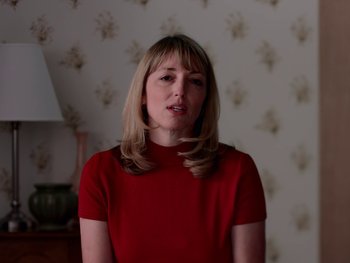 Movie still from “Casting JonBenet” (2017), directed by Kitty Green – A woman in a red shirt is standing in a room; Medium shot, Low angle